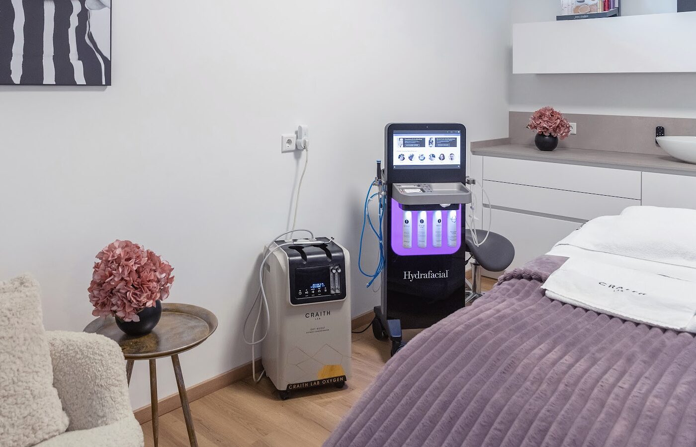 Behandlungsraum im Beautyloft: das HydraFacial-Gerät neben der Liege mit mauvefarbener Decke, daneben Hortensien